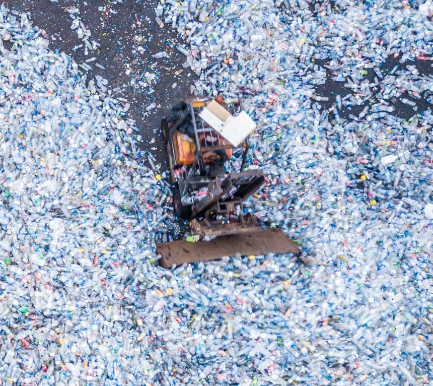 Loader moving baled plastic bottles across a recycling yard, seen from above