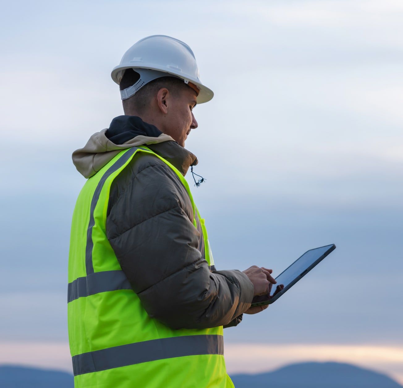 Engineer in a hard hat and hi-vis jacket checking a tablet on site